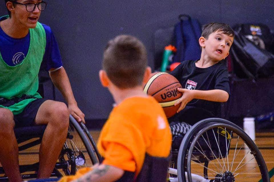 Young boy in wheelchair holds the basketball to pass to teammate.