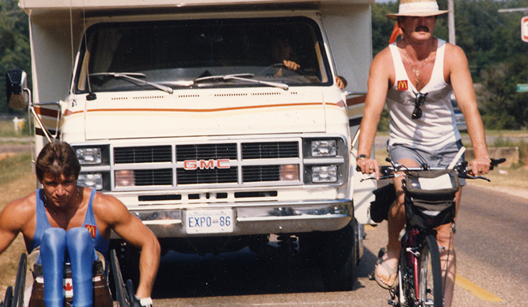 Rick Hansen and Robin Gibson on bicycle going through a road 
