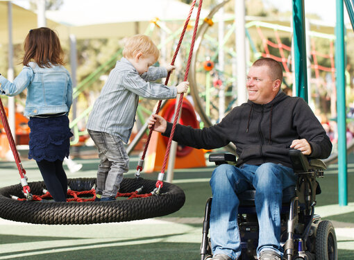 Man using a wheelchair in inclusive playground with two children 