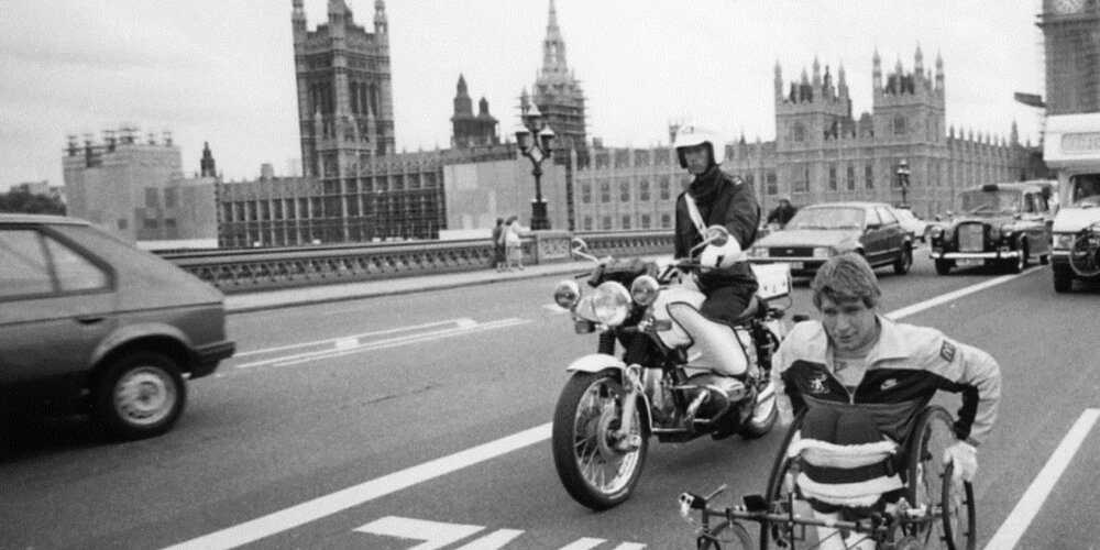 Rick Hansen wheeling past Big Ben alongside Amanda Reid, with a police escort in London, England during the world tour.