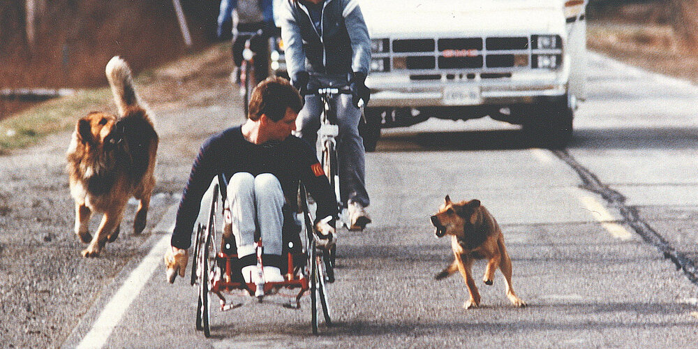 Rick Hansen being chased by dogs during the start of the World Tour in Washington State.