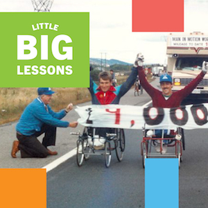 Rick Hansen crosses together with another friend in a wheelchair through a handheld banner with "19,000" written on it on a highway during the Man In Motion World Tour. Little Big Lessons logo text.