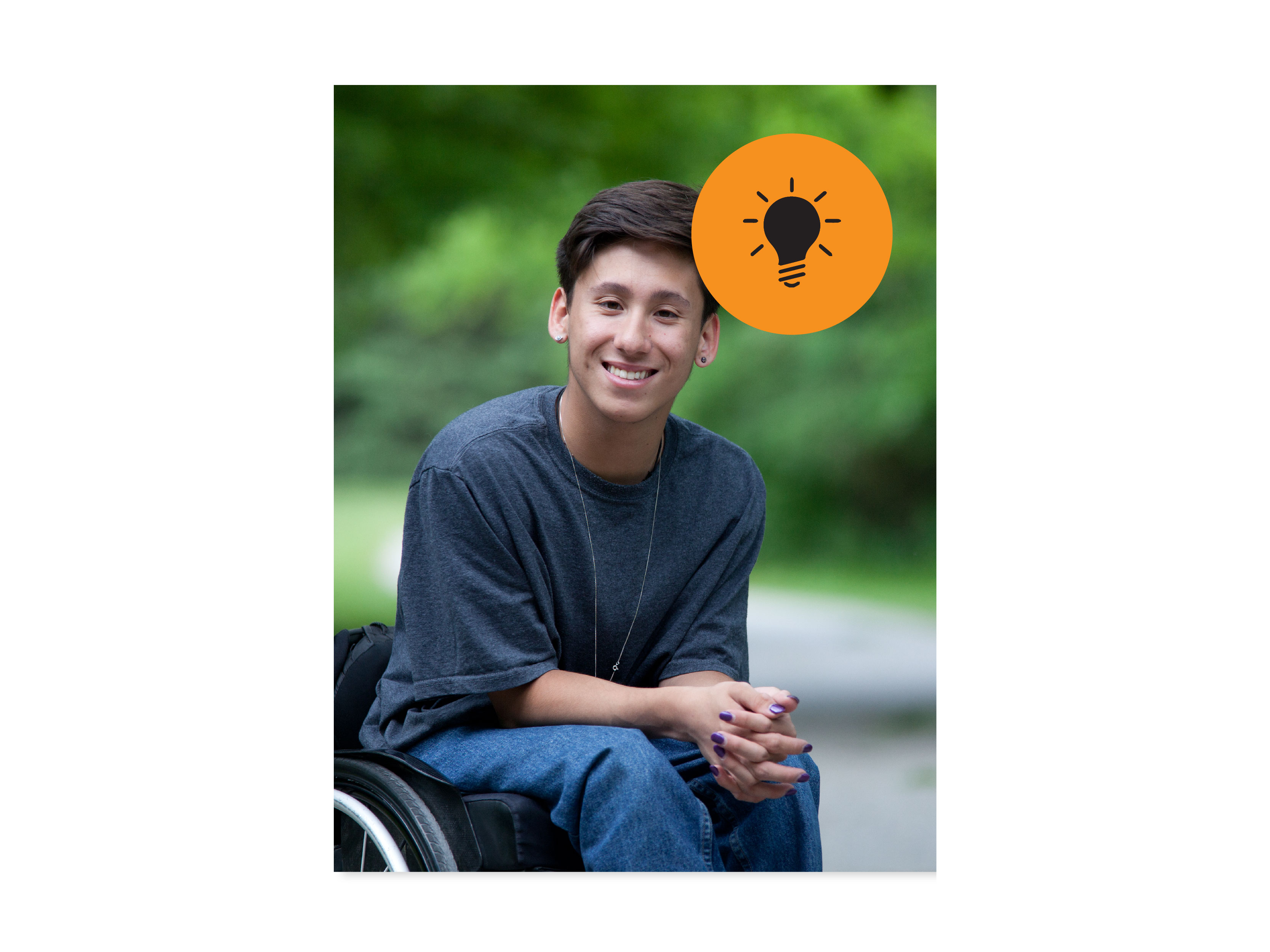 Young adult with dark brown hair, wearing a grey t-shirt and blue jeans, photographed in their wheelchair outside. The greenery in the background is blurred.