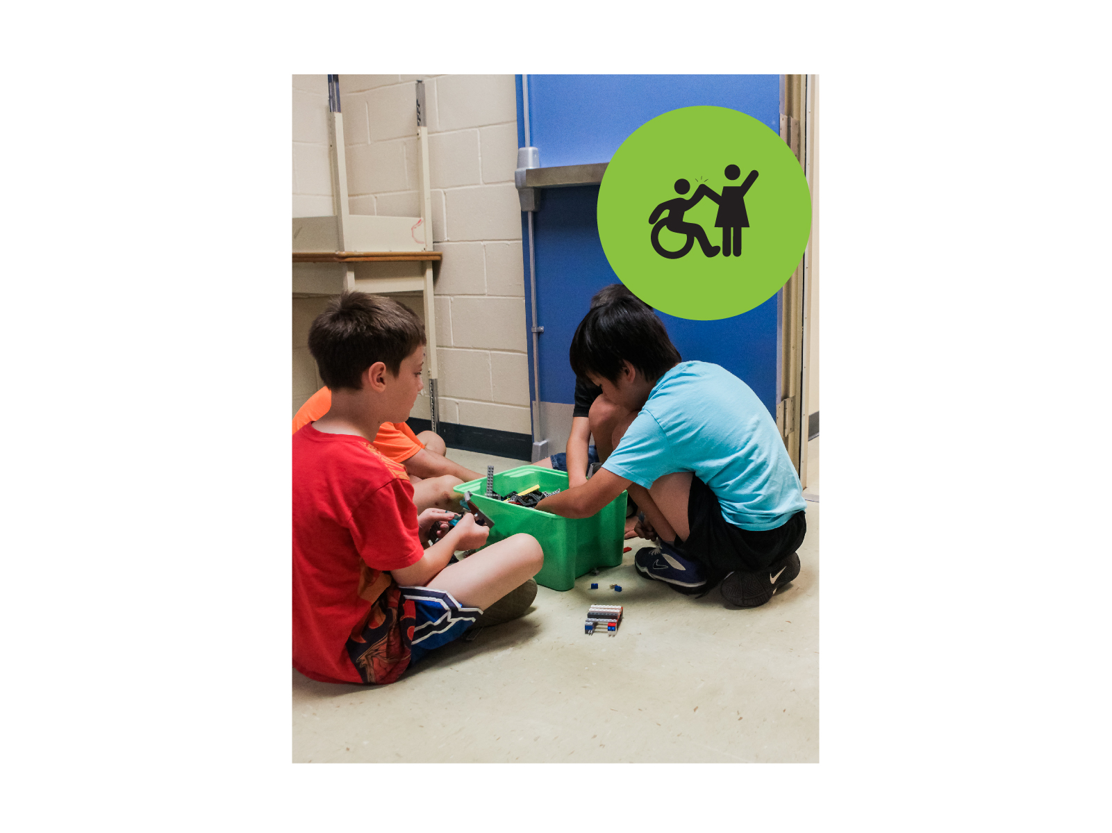 3 boys sitting around a box of legos. Green circle icon with graphic of person in a wheelchair highfiving a person standing up.