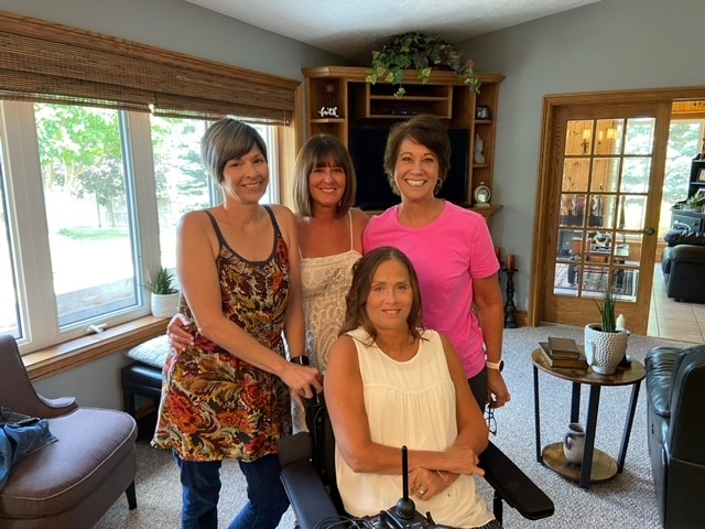 Four women indoors posing for a photo, smiling, one using a wheelchair