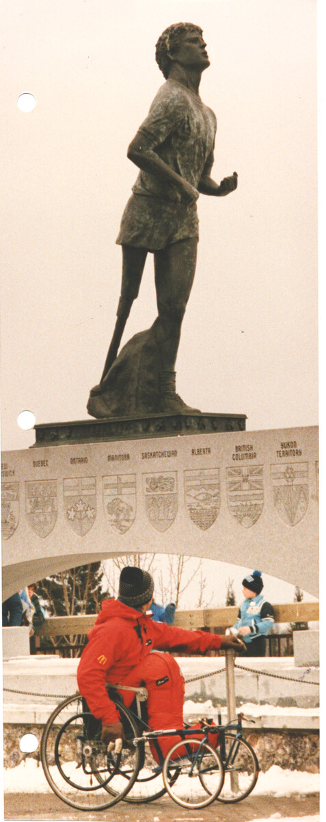 Rick Hansen during the Man In Motion World Tour looking up as he passes a large statue of Terry Fox.