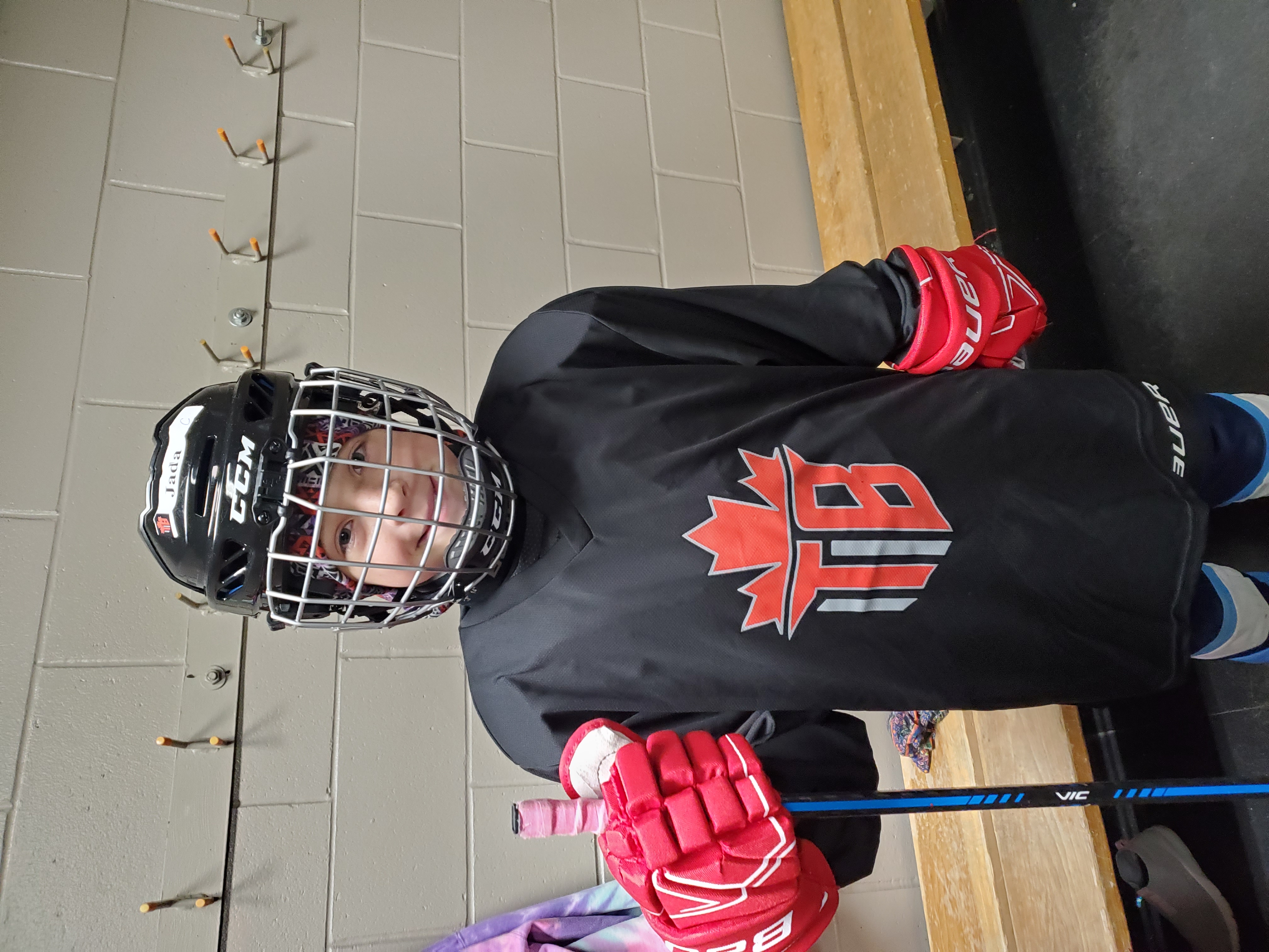 young girl in ice hockey equipment next to a brick wall