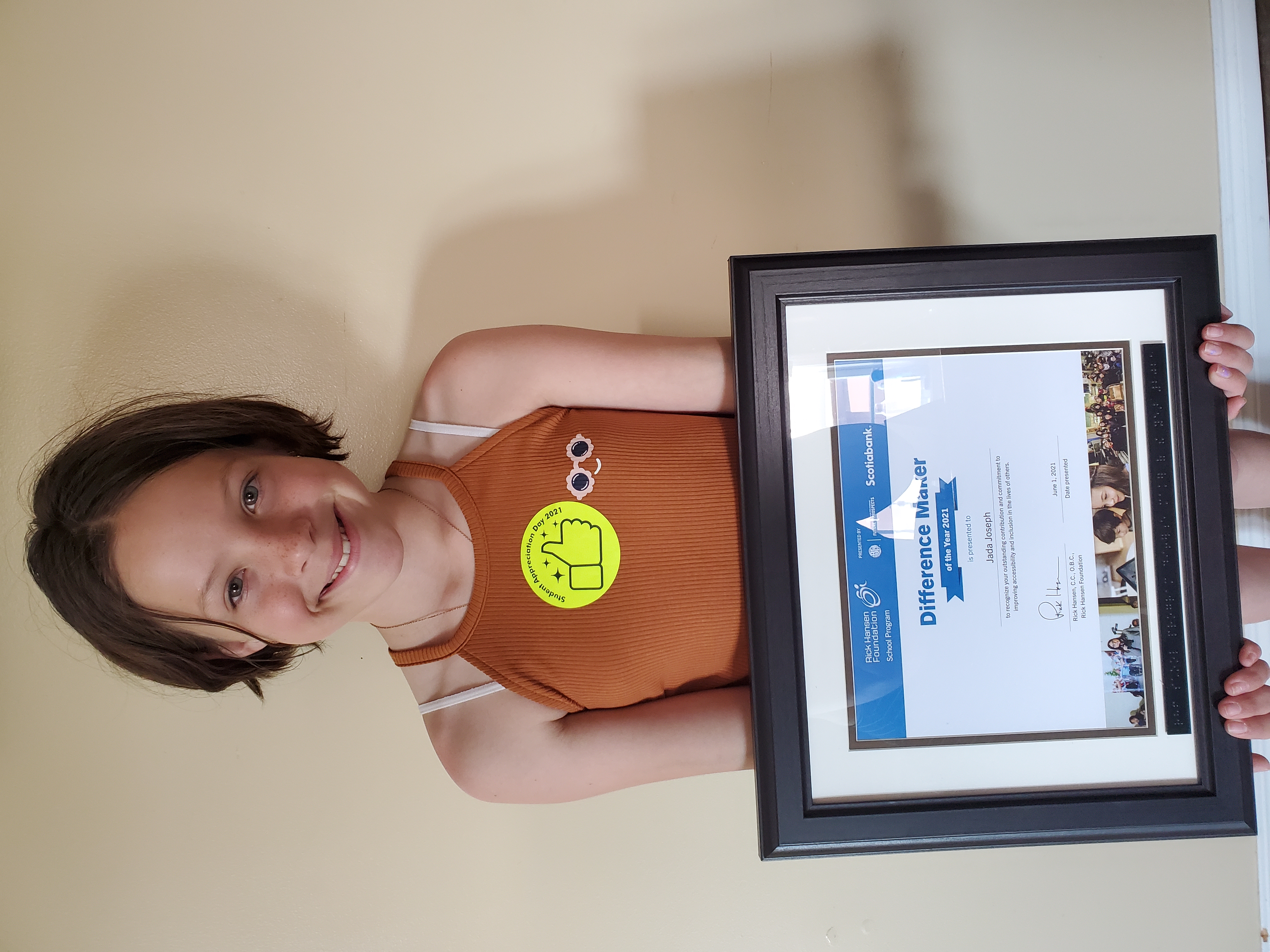 young girl holds a difference maker award certificate in a frame