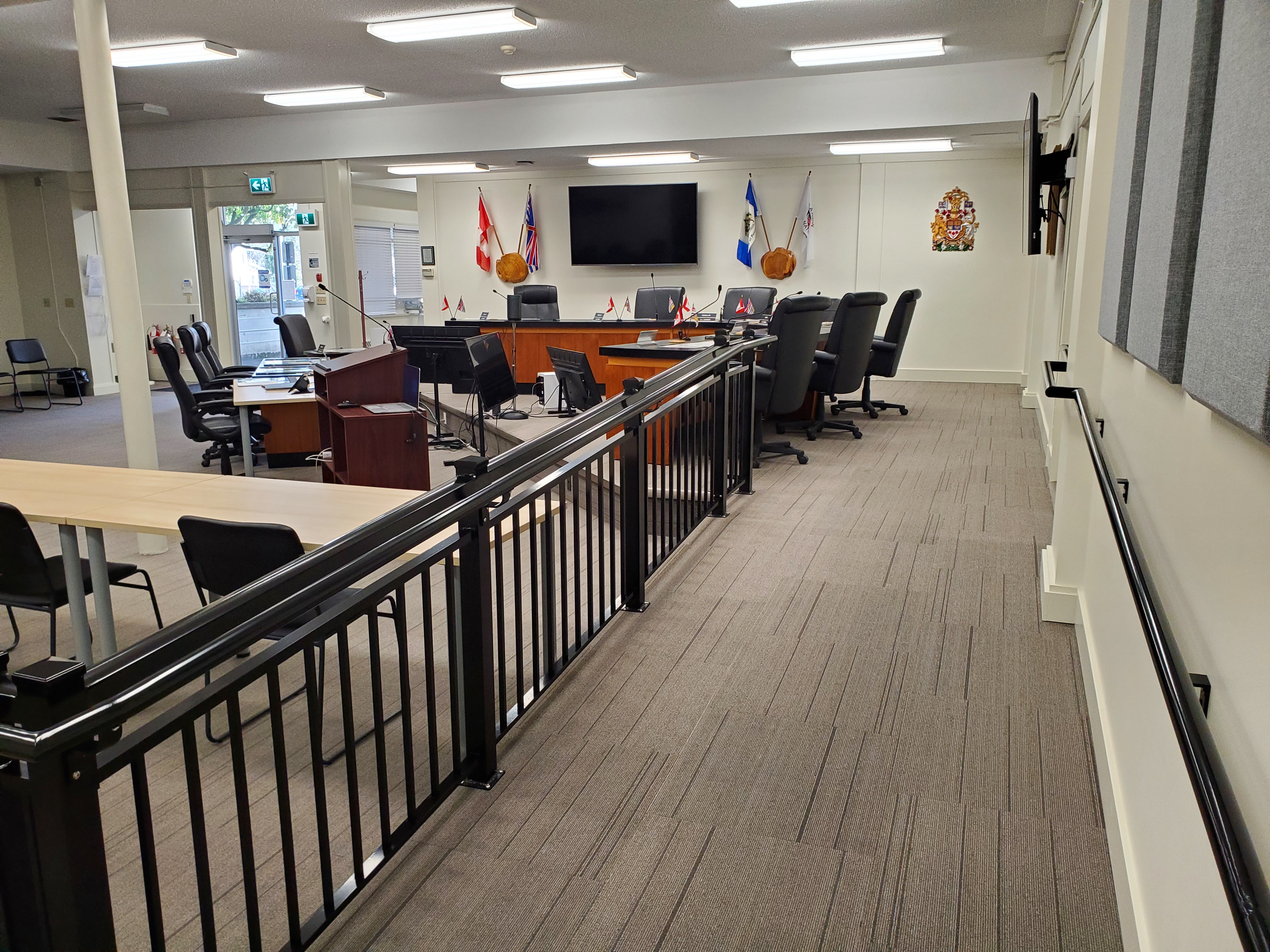 A ramp is in the foreground that leads to the Power River City Council desks in the Council Chambers. Black railings and carpeted floors. The accessible entrance is in the background.
