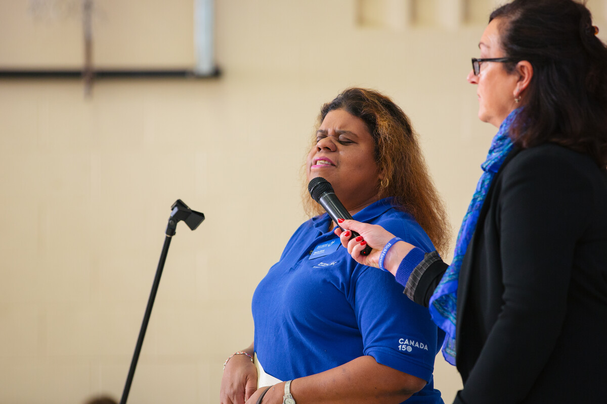 An RHF Ambassador wearing a blue RHF t-shirt giving a presentation. A person with long black hair is holding a microphone up to the Ambassador, 