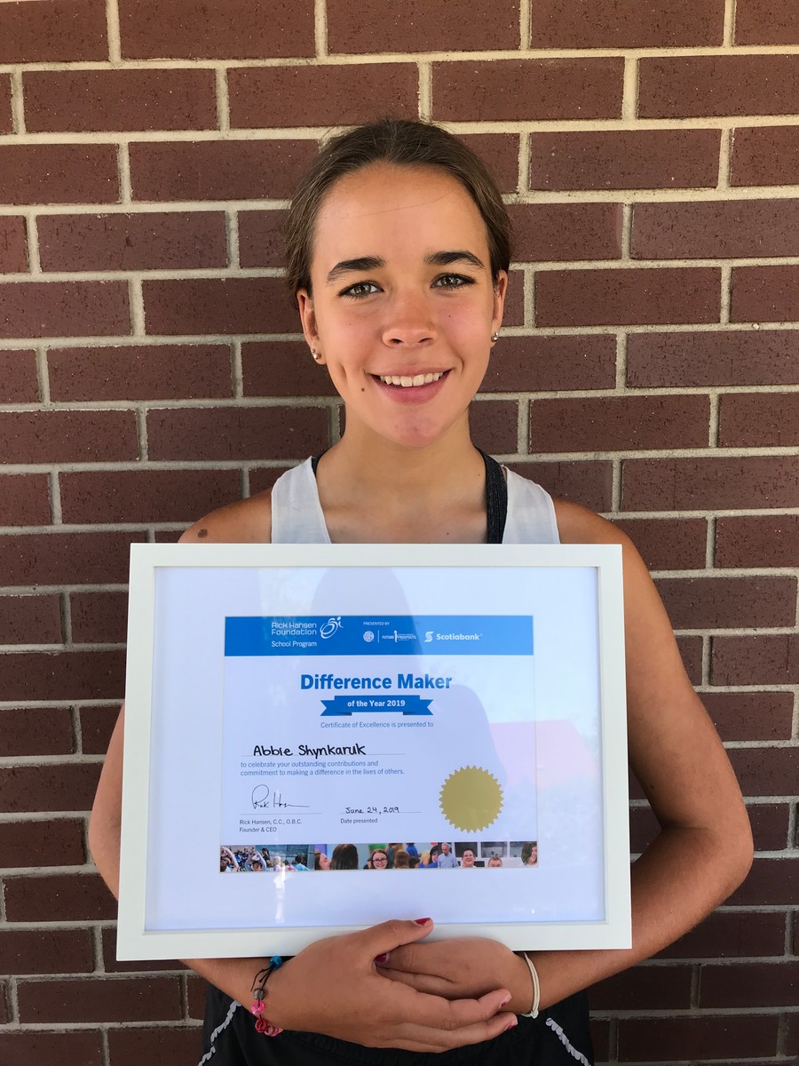 Young girl with brown hair smiling with her certificate, brick background