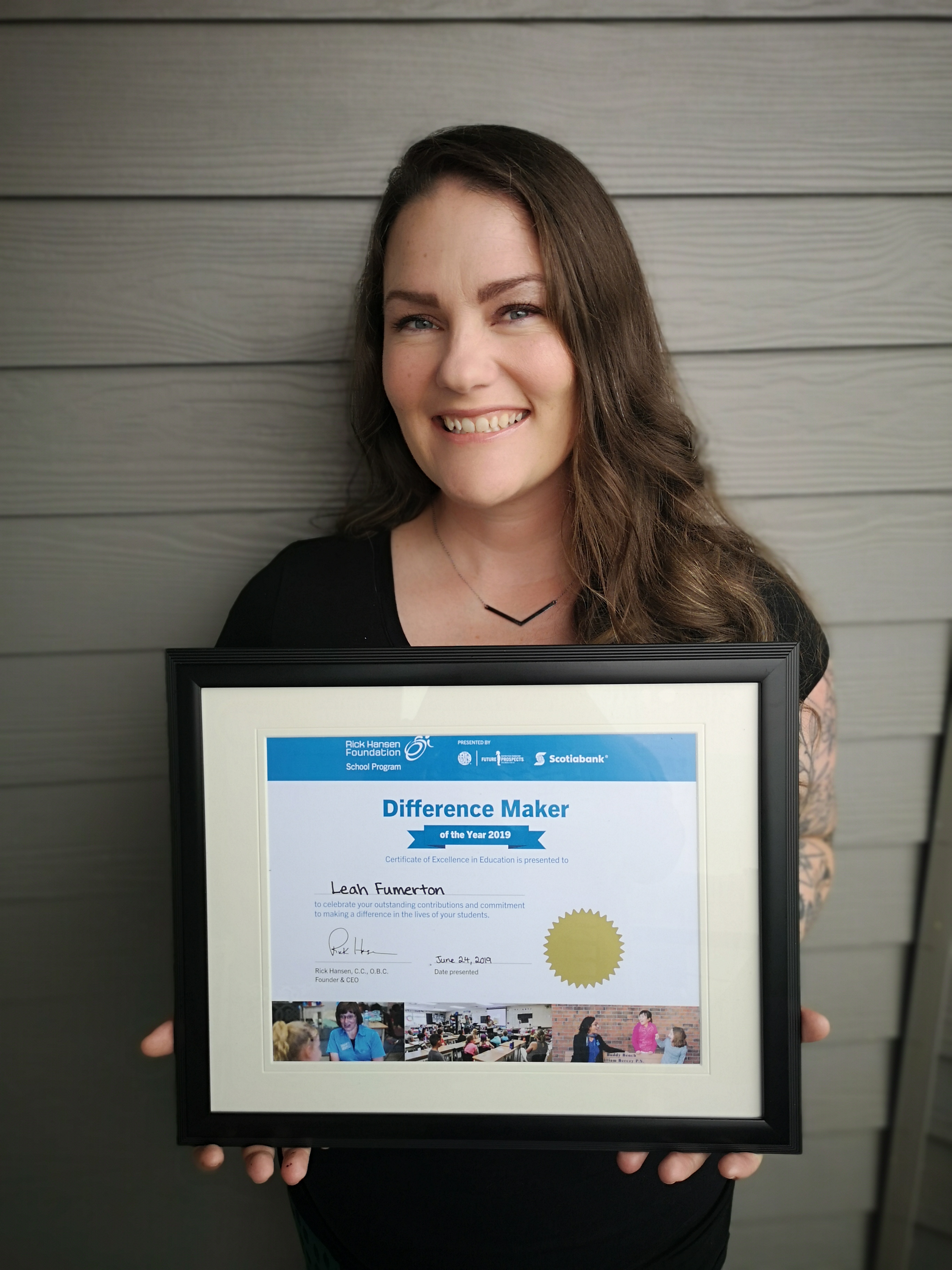 Young woman with brown hair smiles holding her certificate.