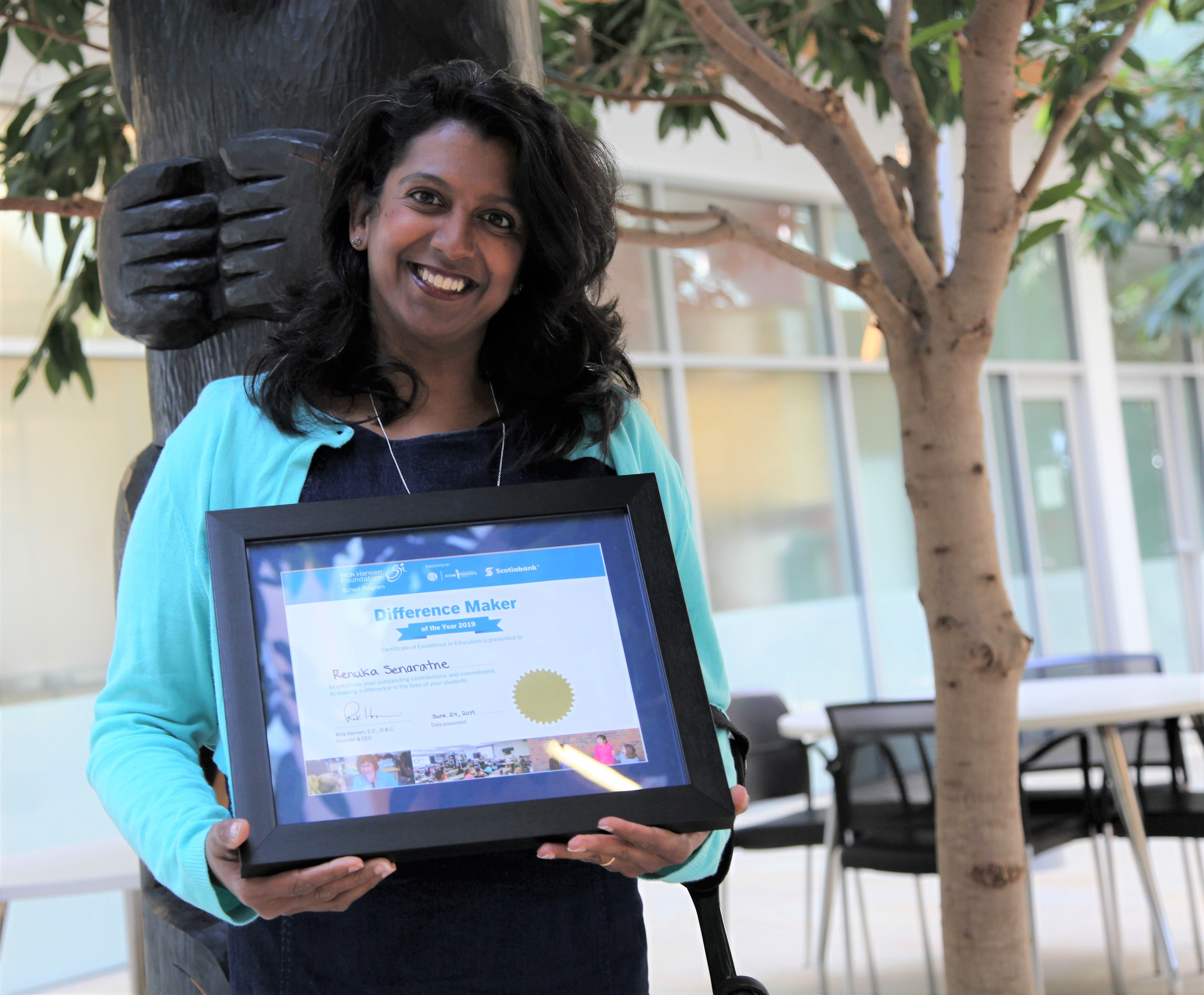 Middle Eastern woman with black hair smiles holding up her DM year certificate. 