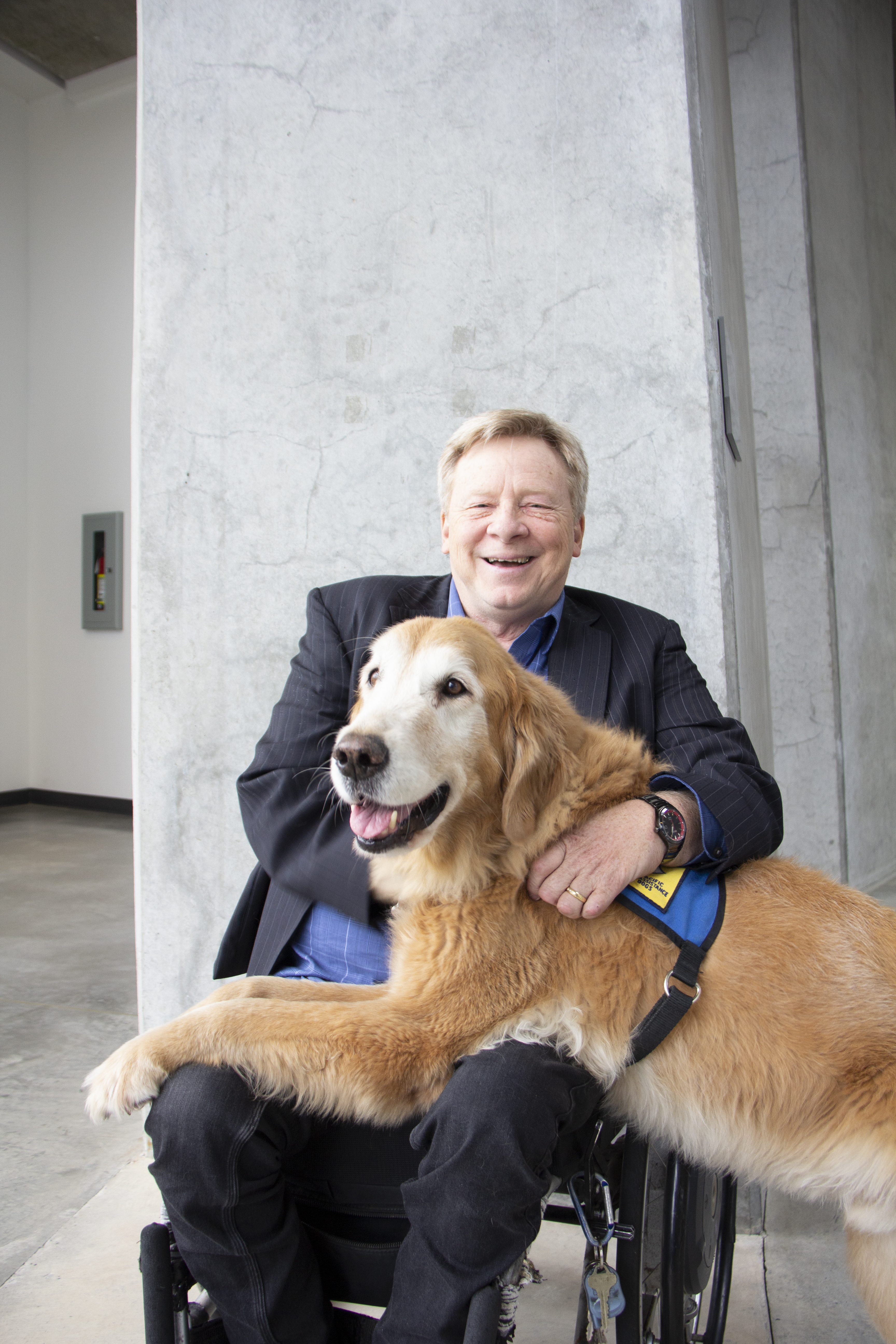 man in a suit using a wheelchair with a service dog on his lap