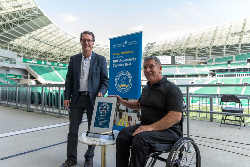 Rick Hansen presenting RHFAC Gold for the Mosaic Stadium alongside Michael Fougere.