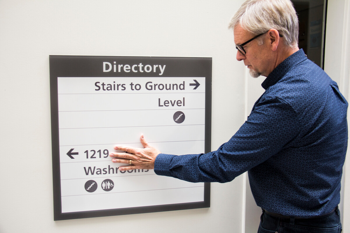 A man reading checking a sign for wayfinding features including raised lettering or colour contrast, among others.