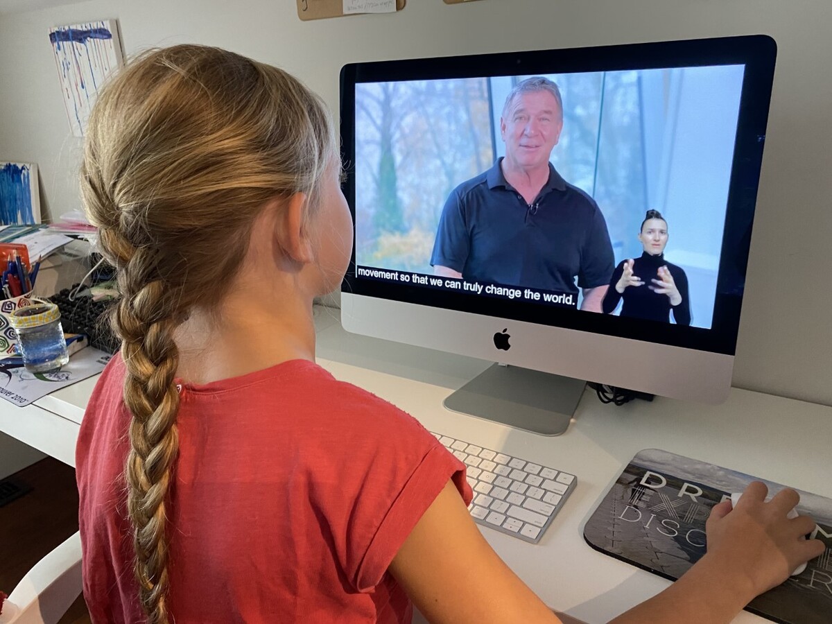 A little girl is seated in front of a screen featuring videos of Rick