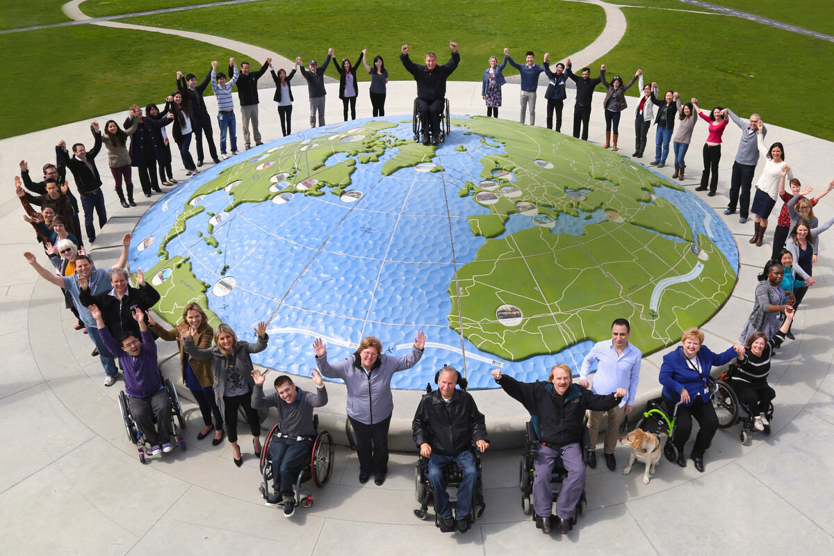 Rick Hansen and the staff of the Rick Hansen Foundation surrounding a large globe with their arms raised triumphantly 