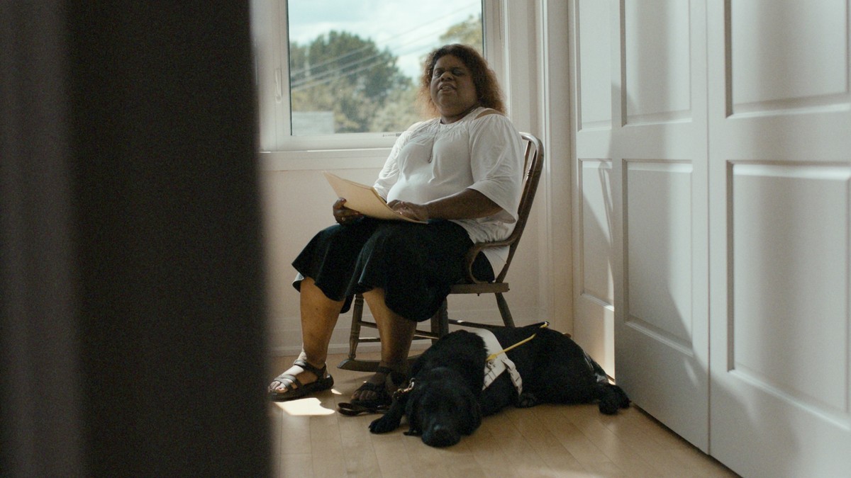 woman by a window with a guide dog reading braille pages with her hands