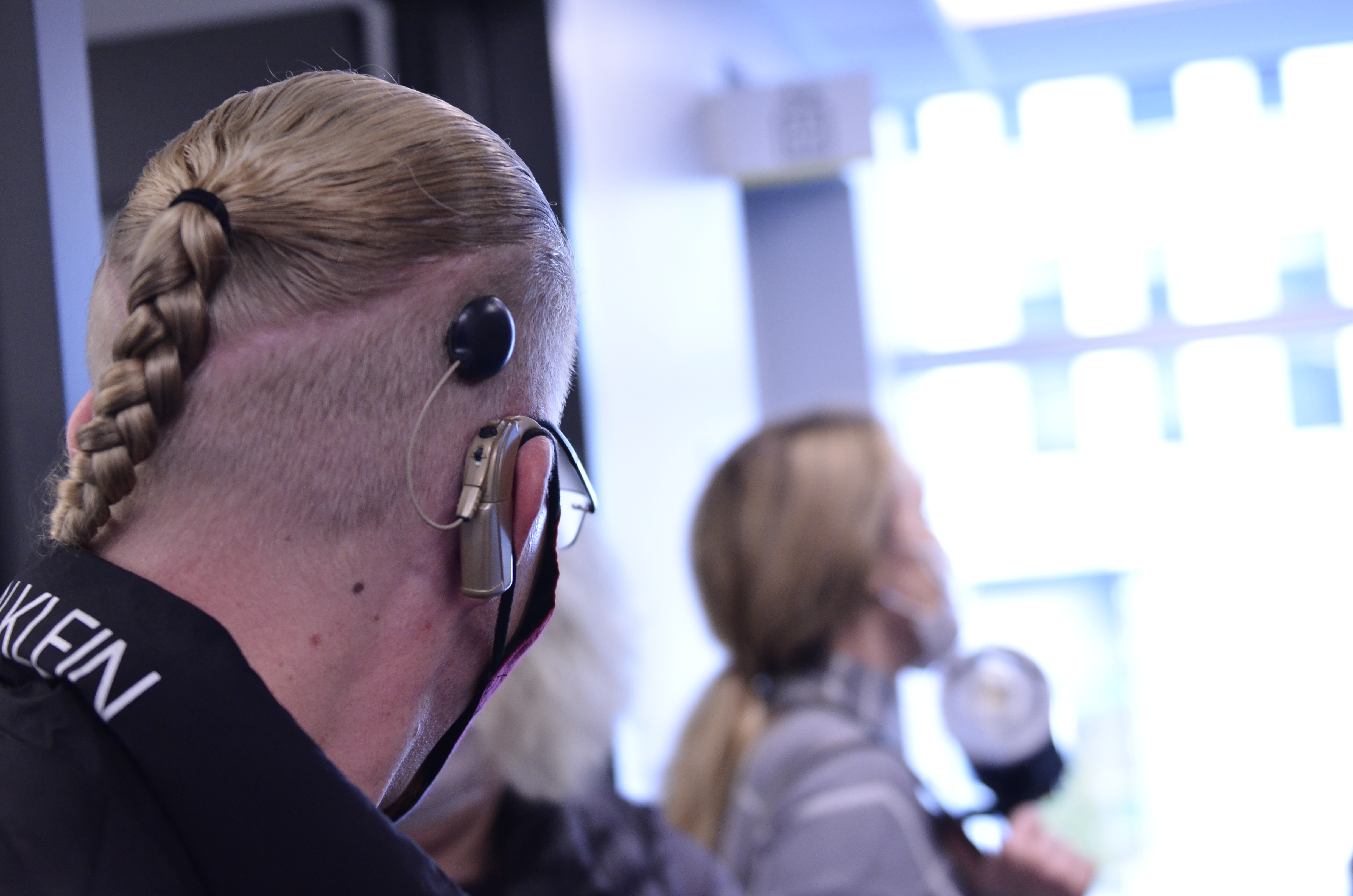 The back of a person's head with braided hair, wearing a hearing aid and glasses.