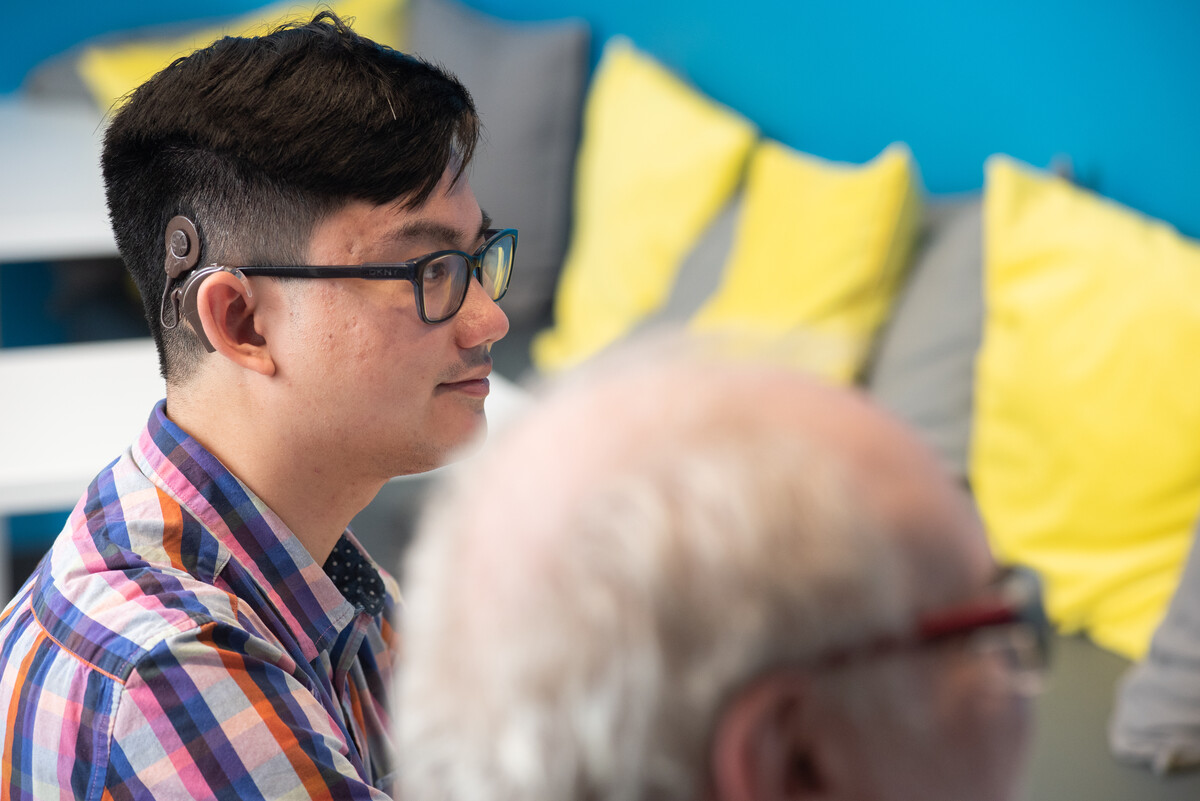 Young man seated indoors wearing a hearing device and glasses