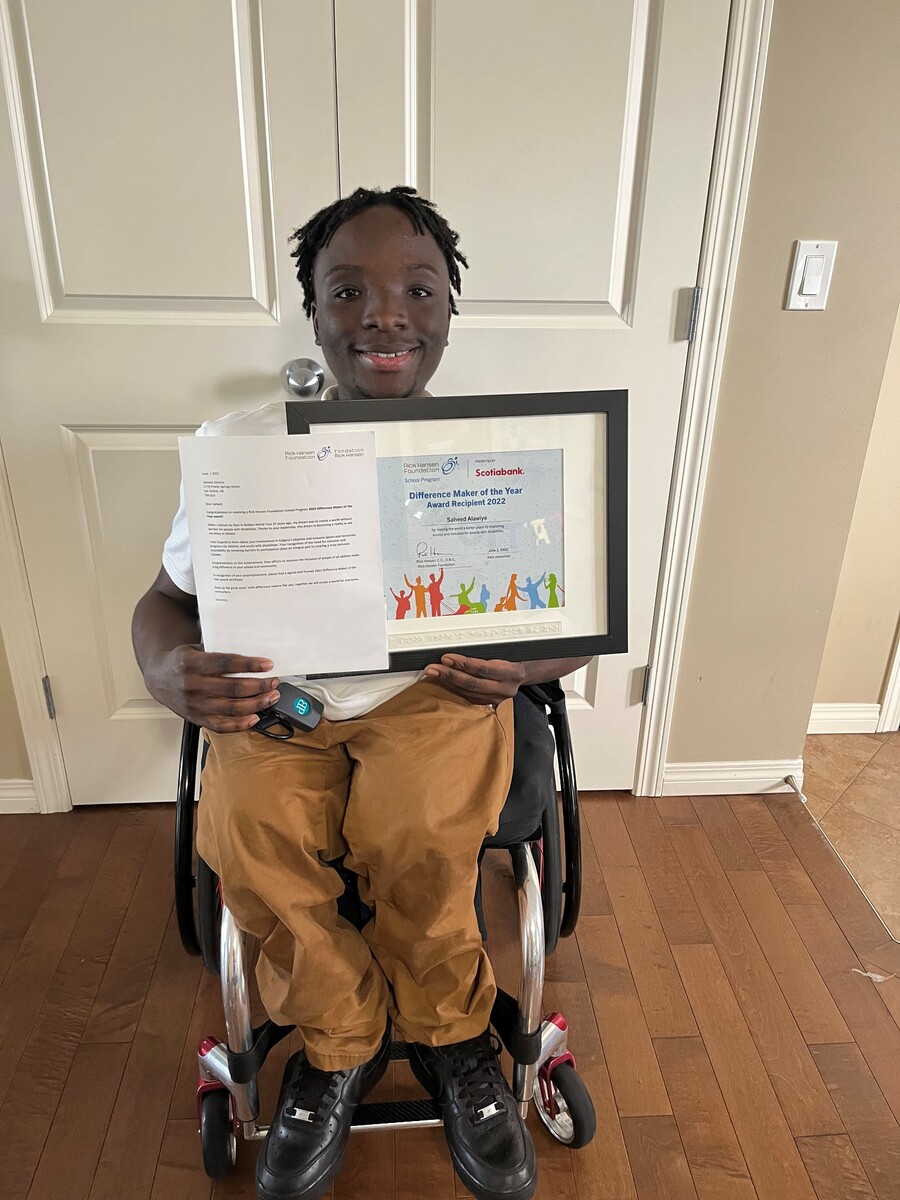 A youth Difference Maker of the Year award recipient holding his award certificate. He is using a wheelchair.