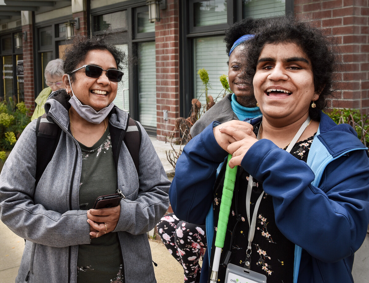 Three people smiling and laughing. One person is holding a white cane that is green on top.