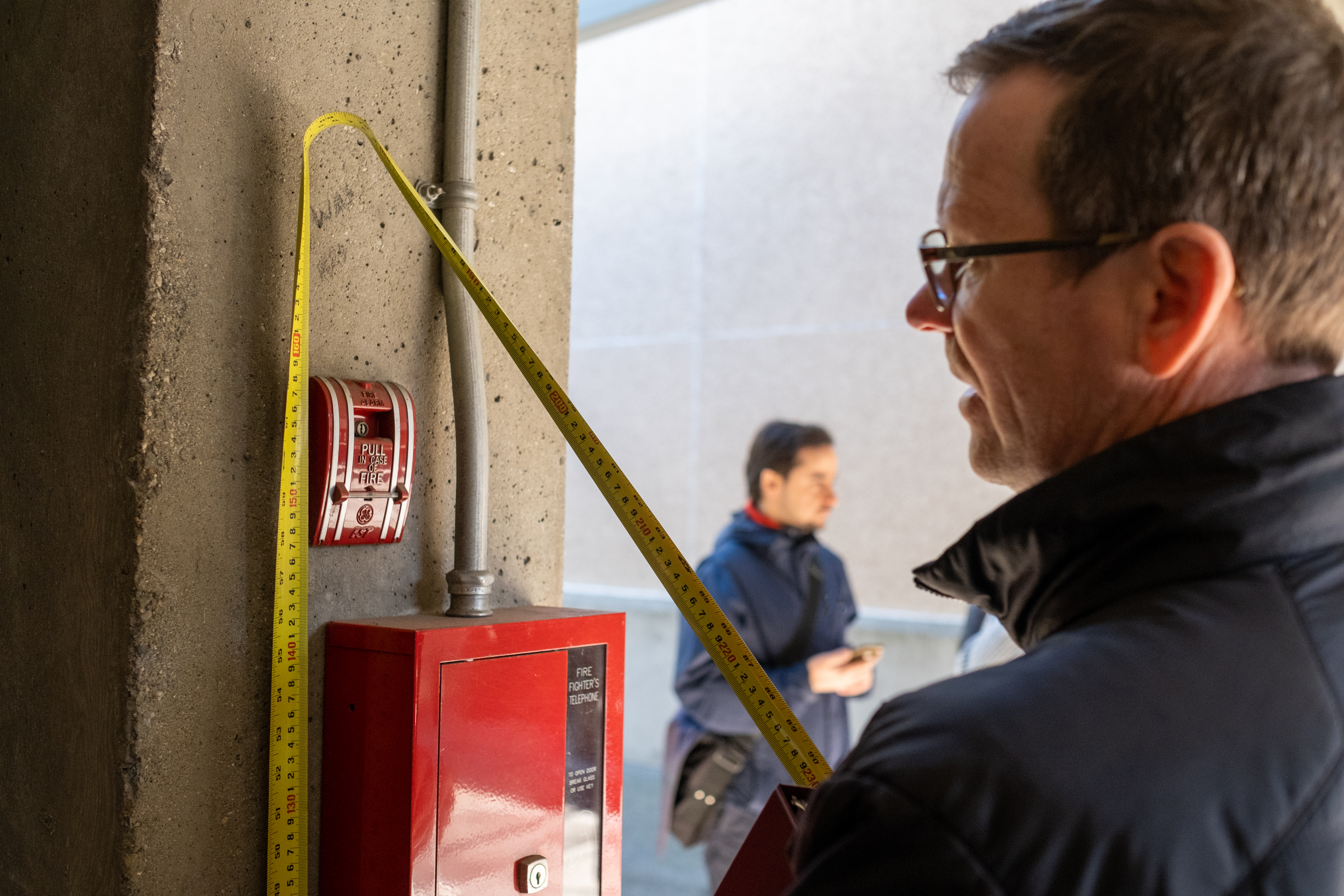 RHFAC Professional measuring a fire alarm mounted on a wall 