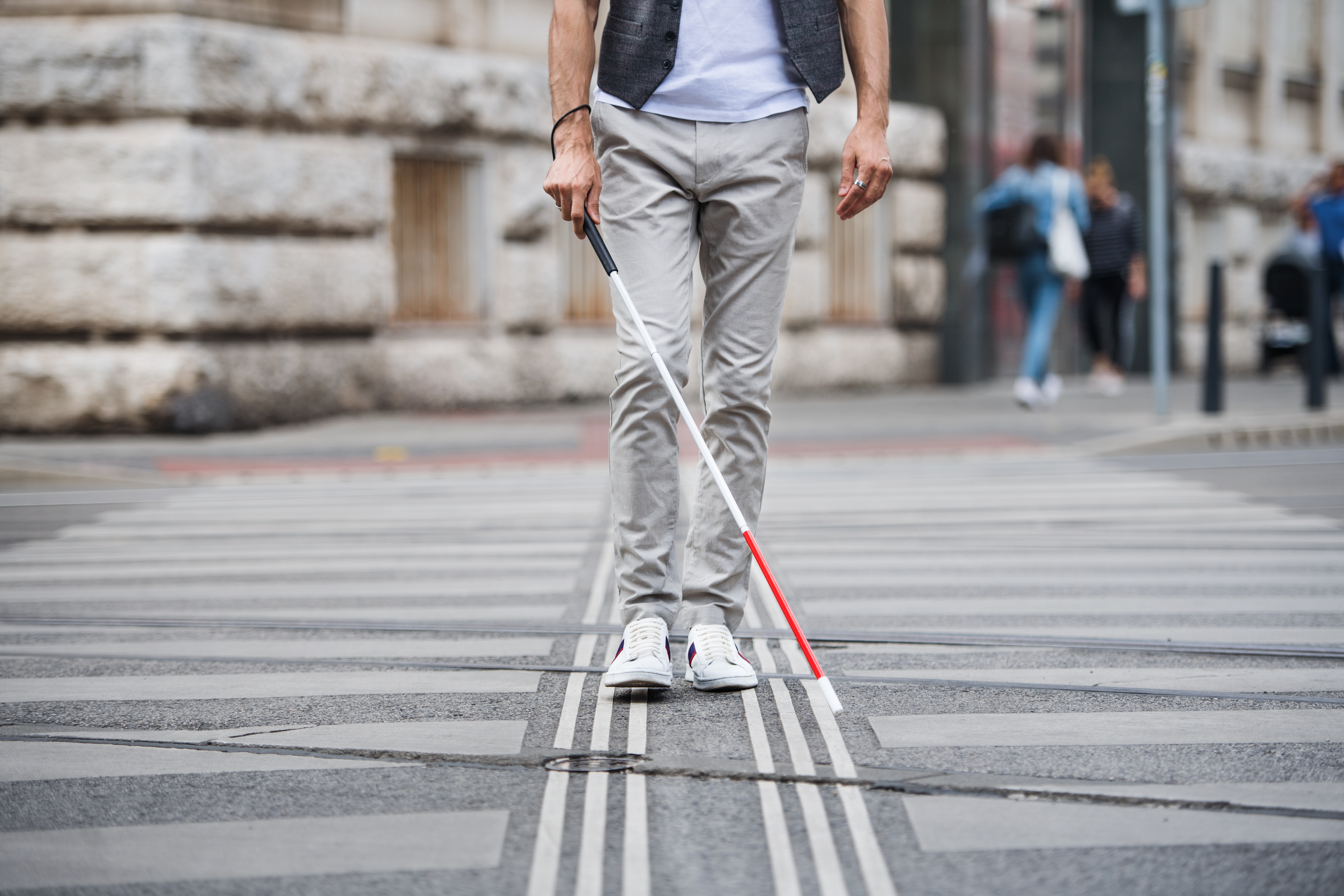 A person walking across a city street using a white cane with a red tip.