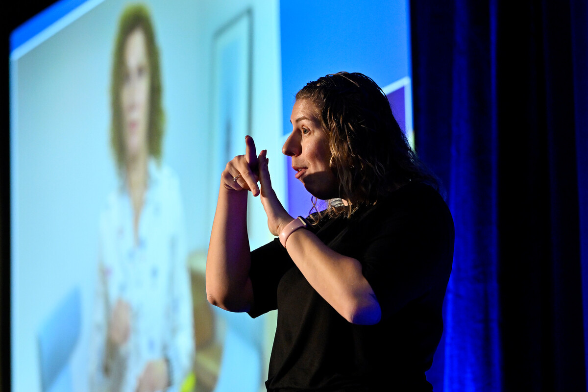 An American Sign Language interpreter in front of a projector screen.