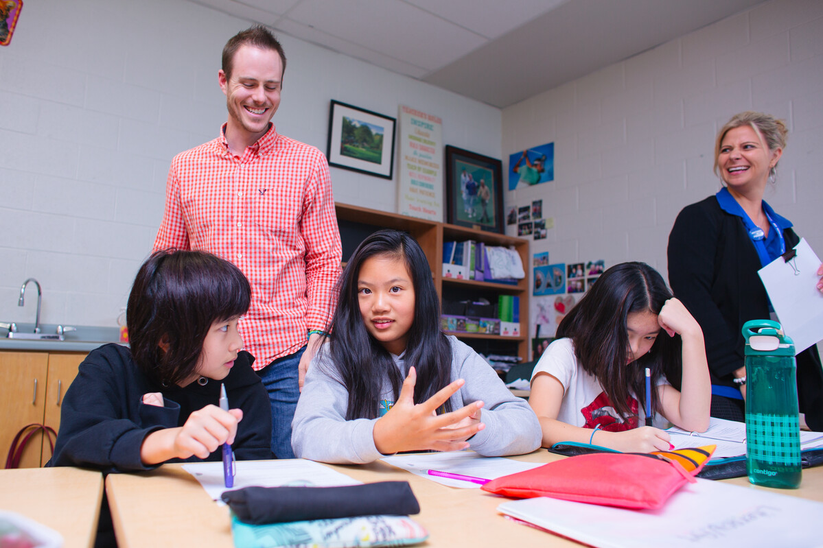 Two educators standing behind a table of students who are working