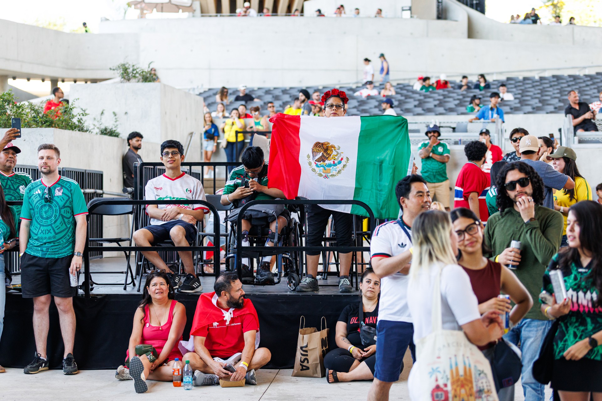 Crowd gathered at FIFA Fan Festival Vancouver, with a person standing on an accessible viewing platform holding a large Mexican flag.