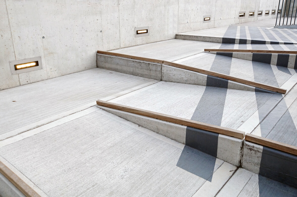 Concrete outdoor ramp system with multiple angled pathways and integrated wooden handrails. 