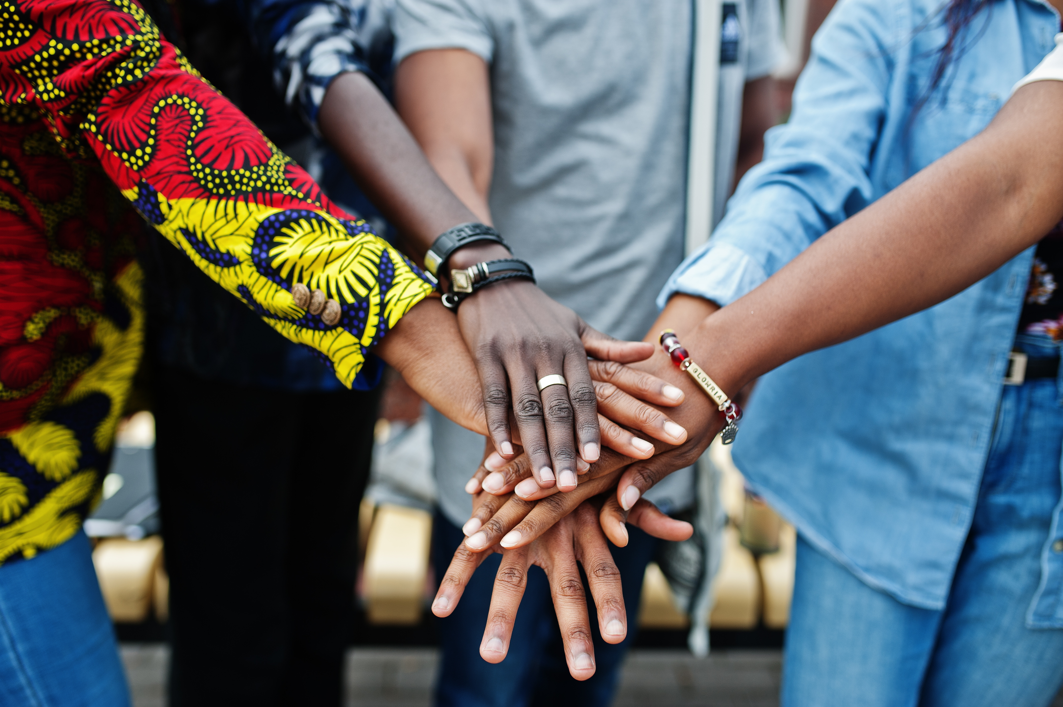 Several people stand together with their hands stacked in the center, showing a range of skin tones 