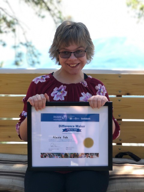 Woman with grey short hair wearing sunglasses in flower shirt smiling holding certificate. 