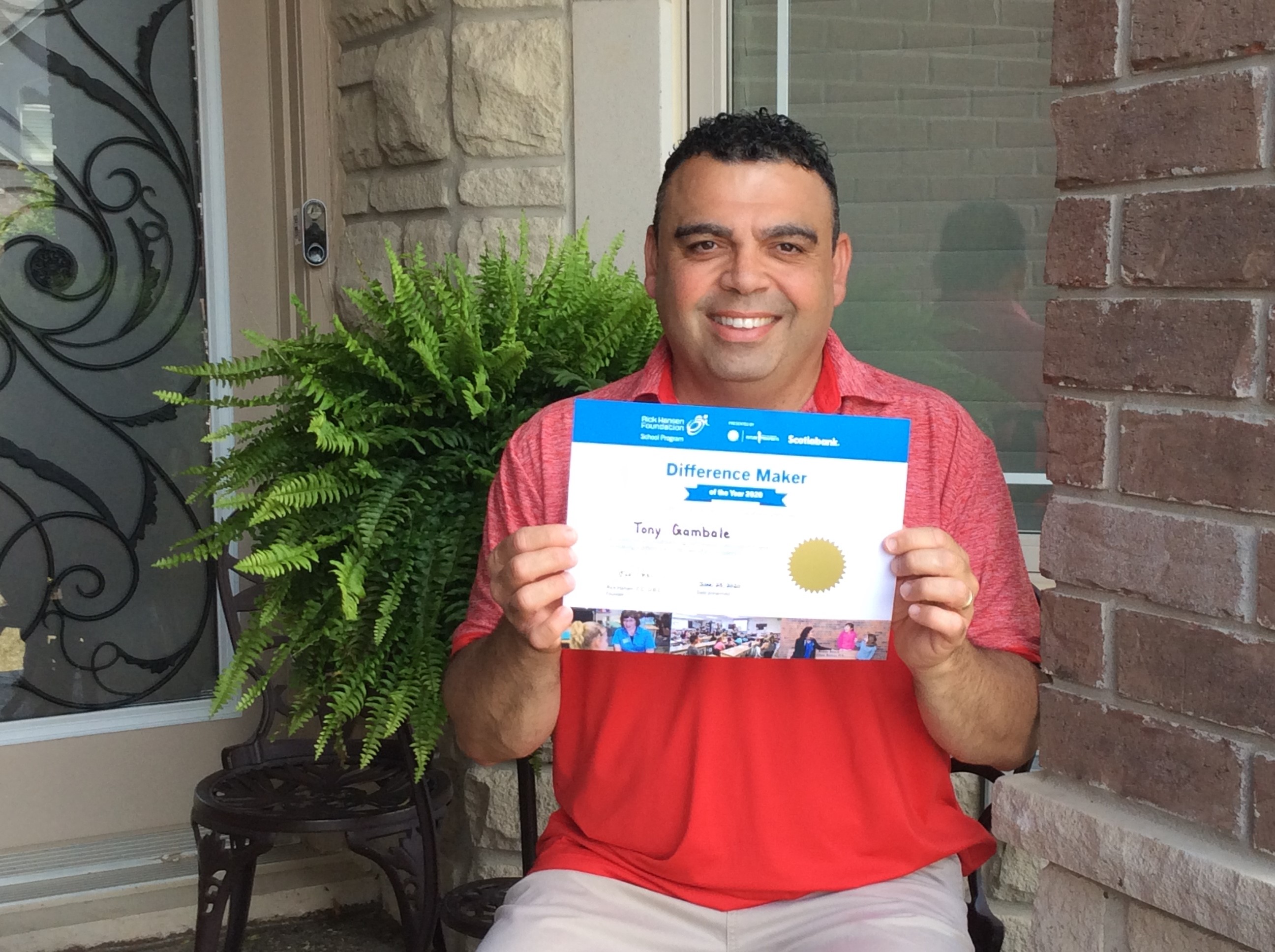 Italian man in red shirt smiling holding his certificate. 