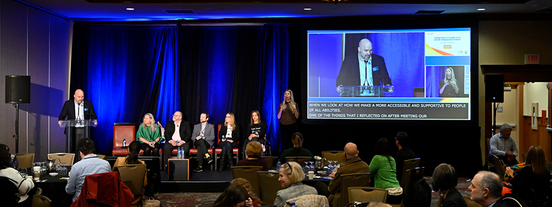 A conference space with the audience facing a panel and projector screen.