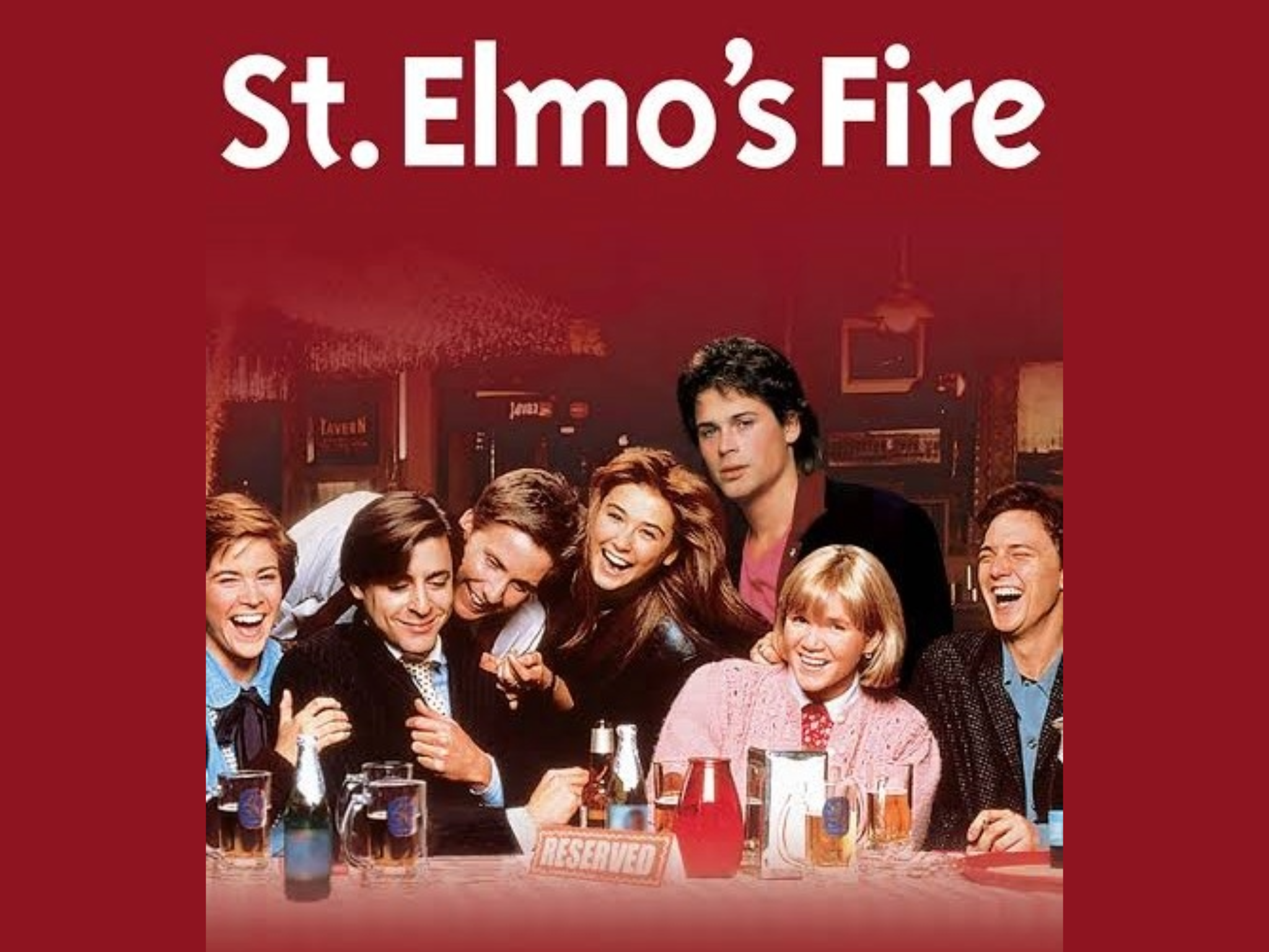 A group of seven people sit closely together at a table covered with various drinks. The background features a bar interior. At the top of the image, large white text reads 'St. Elmo's Fire' against a solid red background