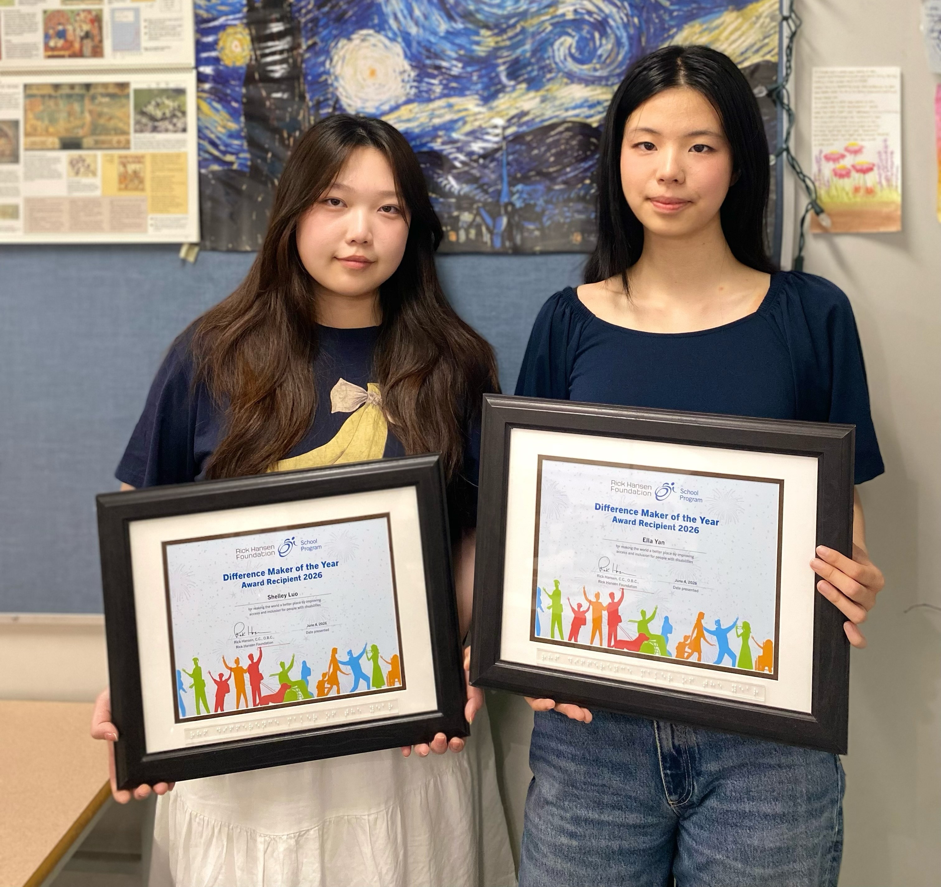 Two young women with long dark hair standing side by side indoors, each holding a framed “Difference Maker of the Year Award Recipient 2026” certificate.