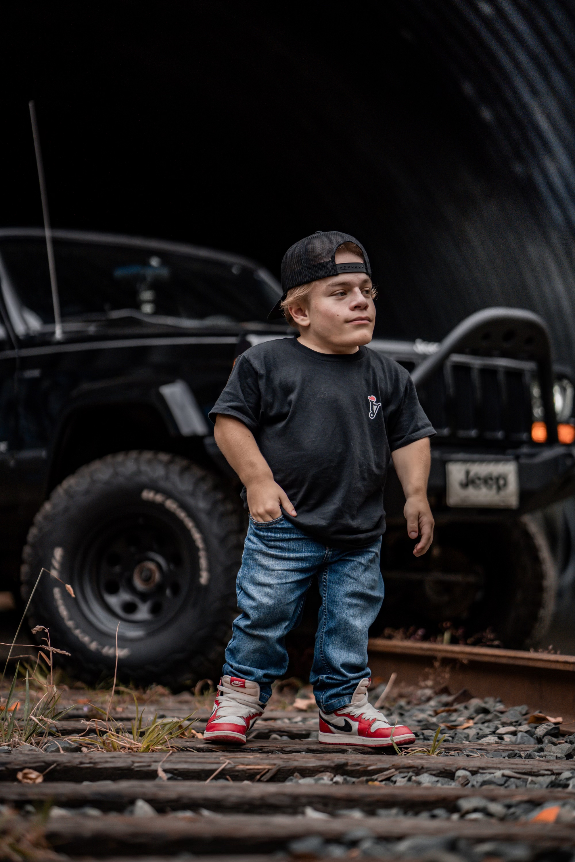 Caden in a black shirt and jeans standing in front of his Jeep