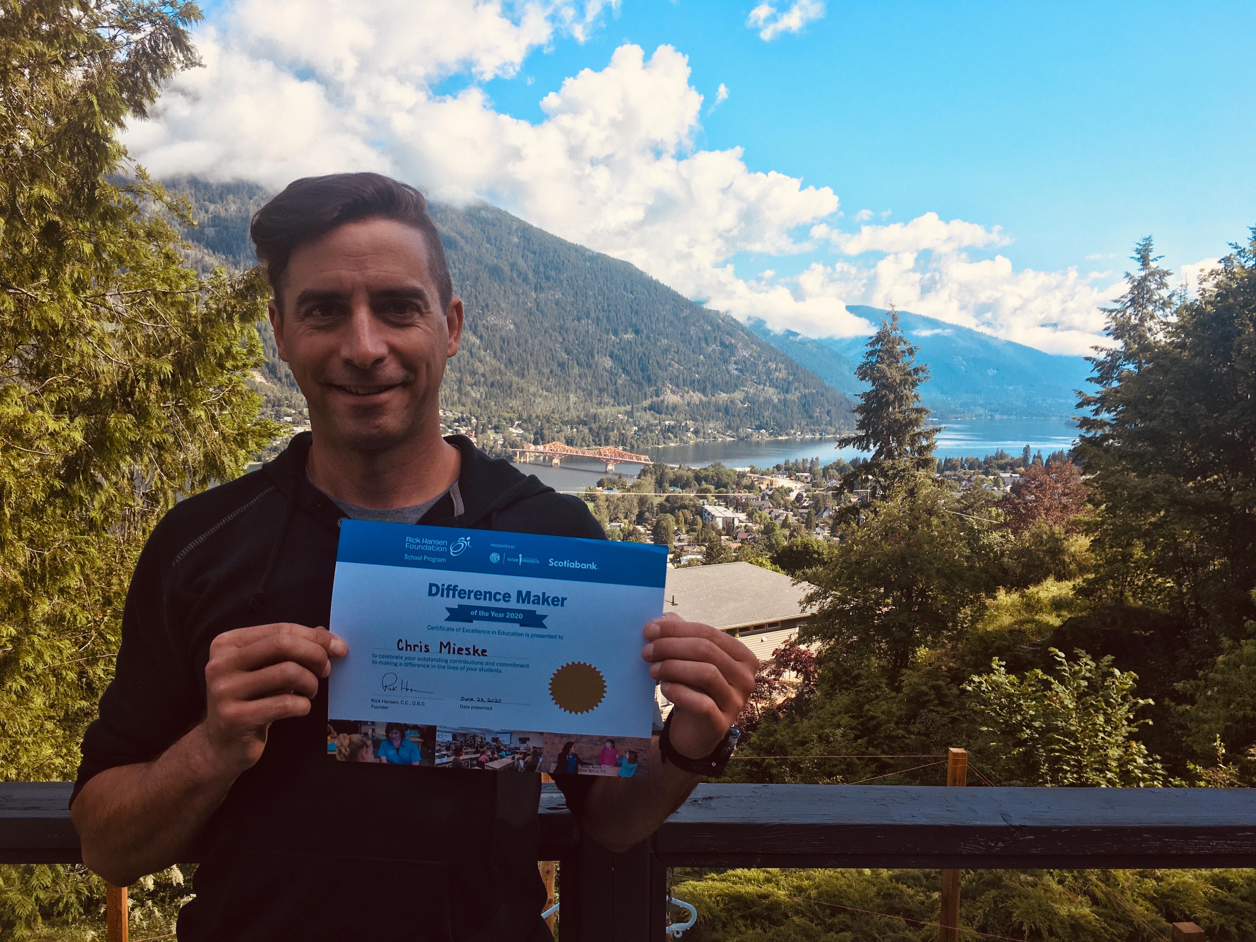 Caucasian Man in the mountains smiles holding up his certificate. 