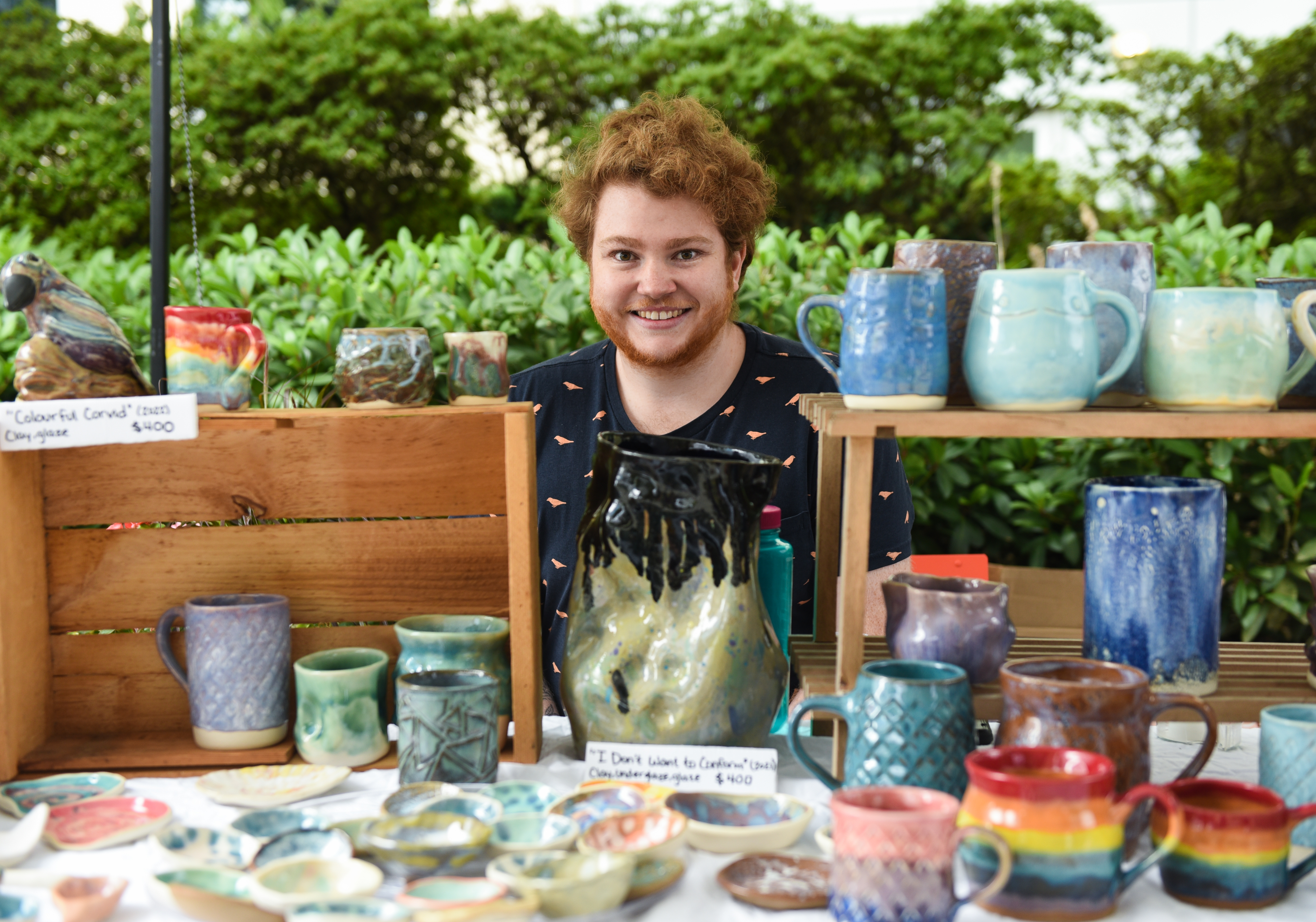 Charlie Sandeman who has short red hair and is wearing a black sleeveless shirt, sitting at a table selling pottery