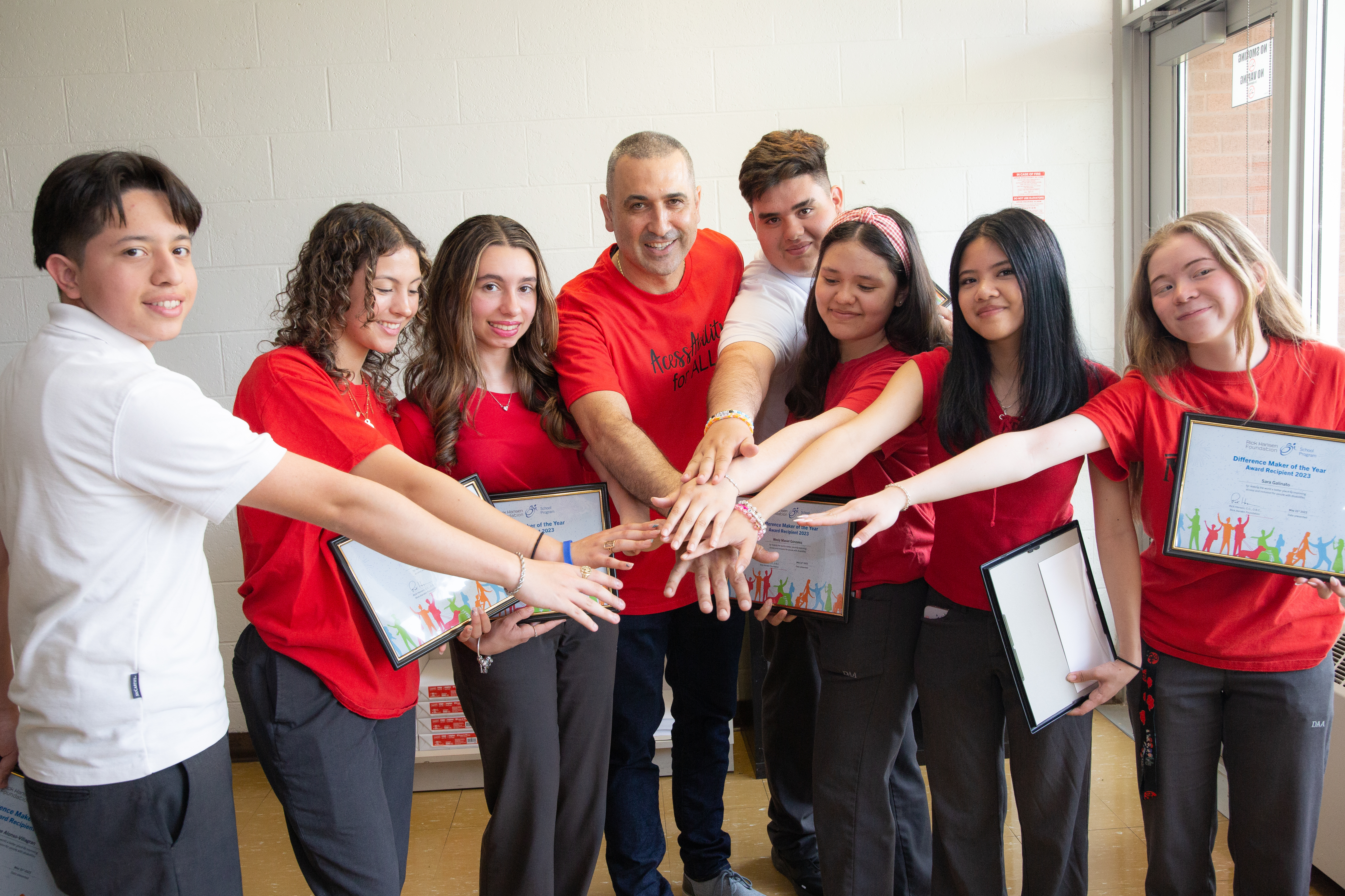 The Dante Accessibility Team with their teacher, Angelo, holding their hands in the centre of a semi-circle. They are all wearing red t-shirts.