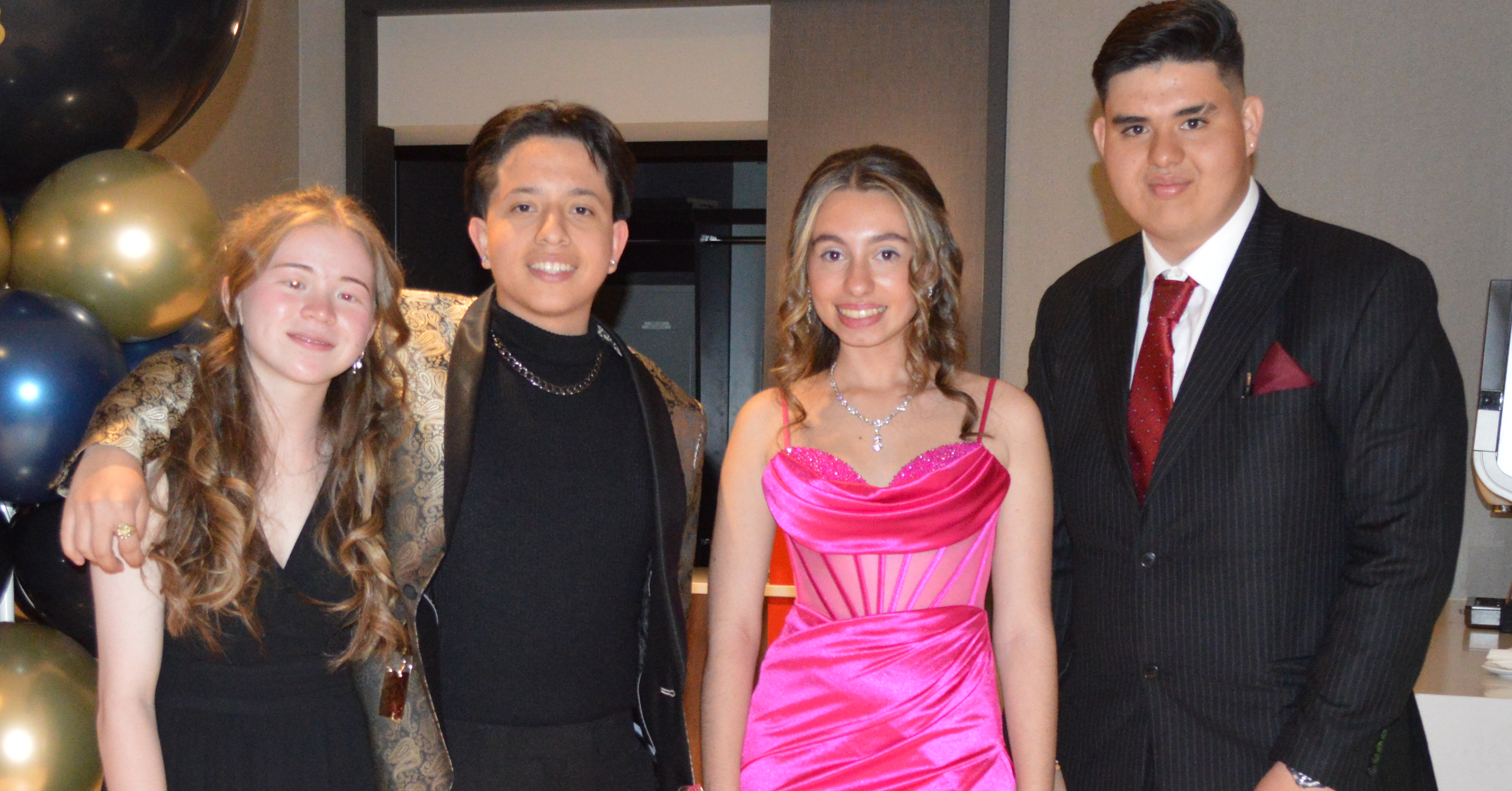 Four young people at a formal event smiling at the camera. Two people are in dresses and two are in suits.