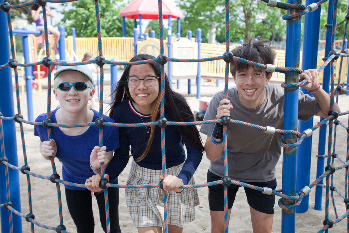 Elena at the park with her brother and sister. The three are looking through a climbing net and smiling