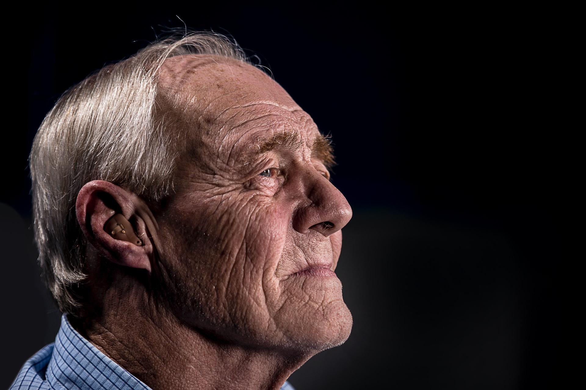 Older man wearing a hearing aid and looking into the distance.