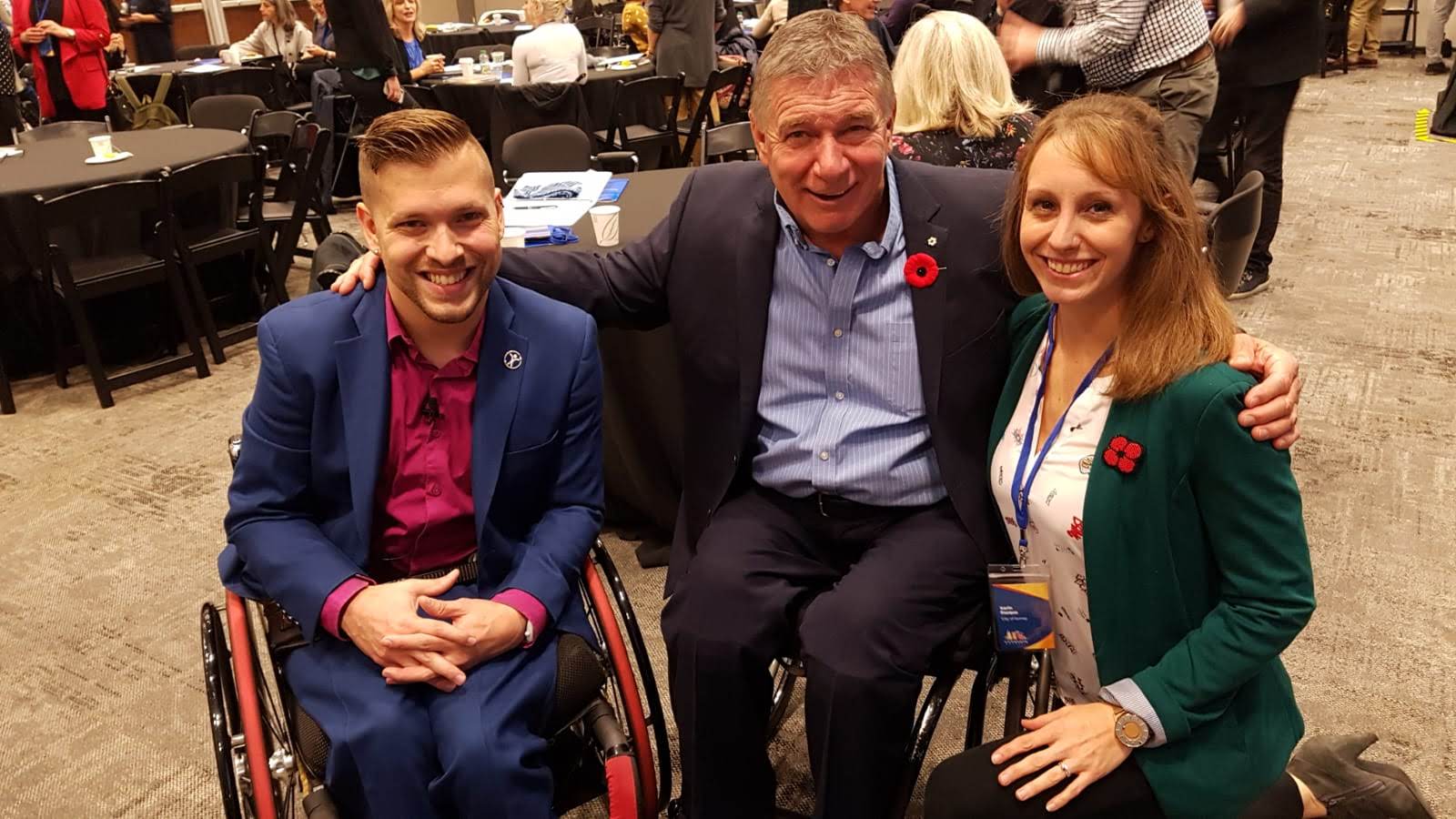 Marco Pasqua and Rick Hansen with a person with long hair and is wearing a green blazer. Marco and Rick are using wheelchairs.