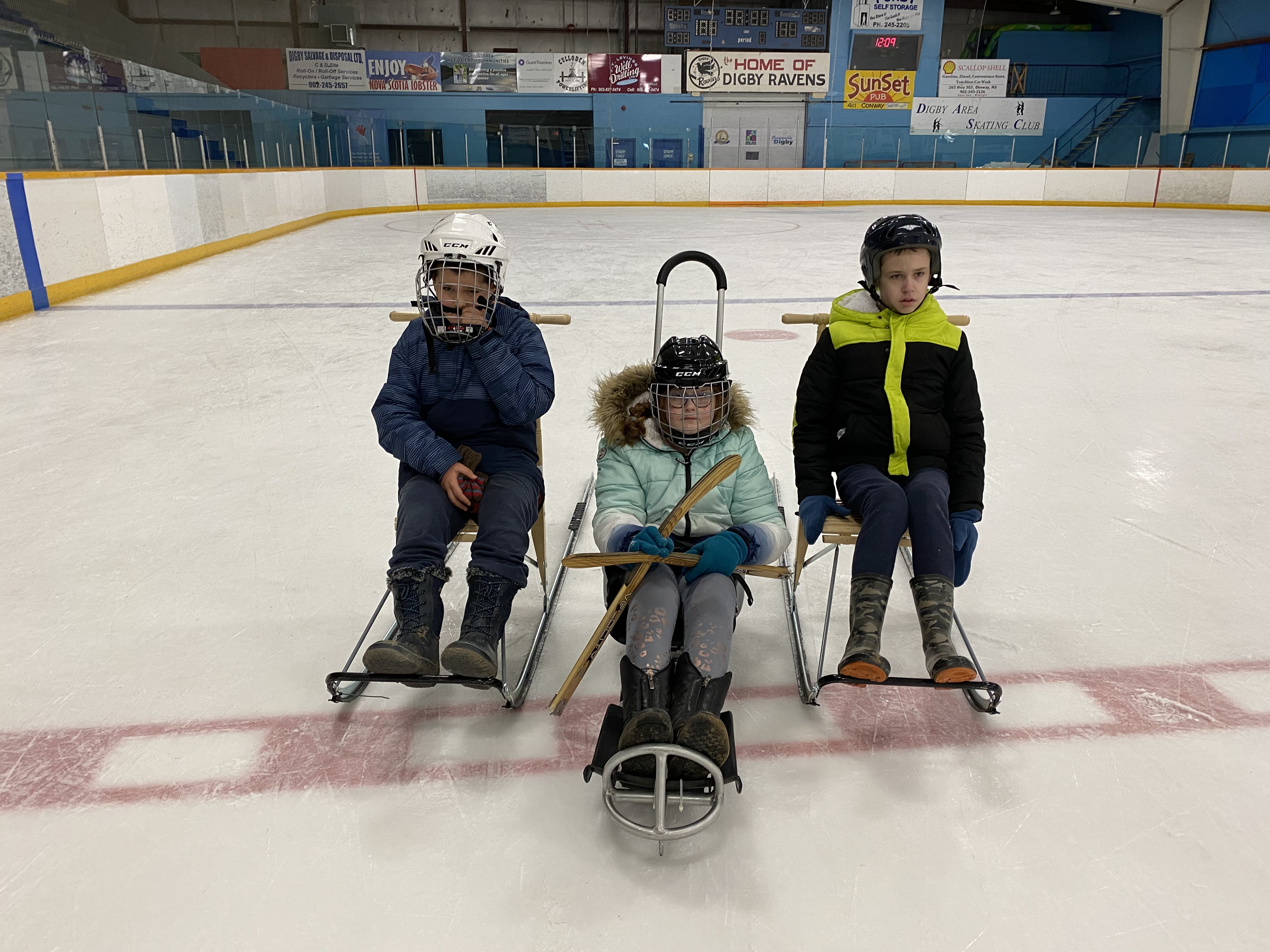 three children using kick sleds on ice rink