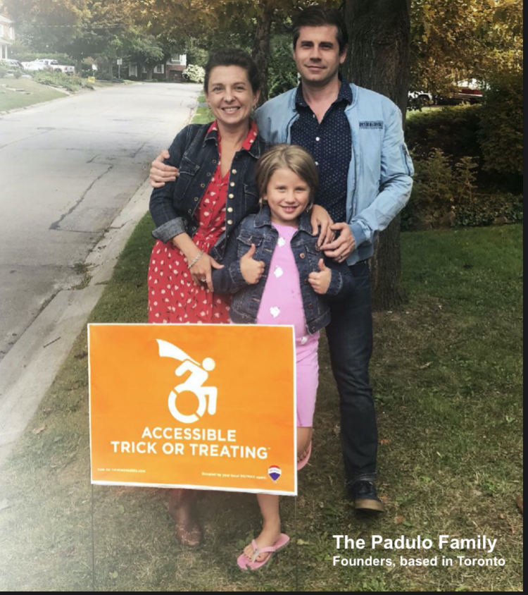 Young girl standing outdoors on a lawn with two thumbs up, with a lawn sign that says accessible trick or treating