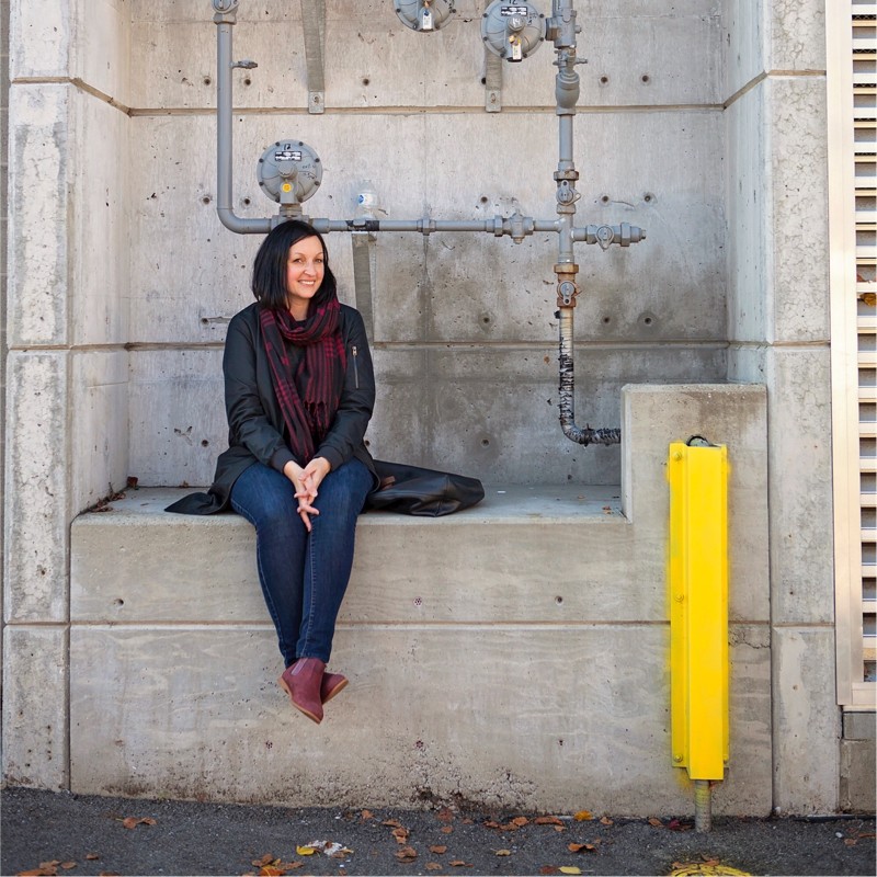 Photo of a stylish woman sitting in a loading bay and smiling at the camera.